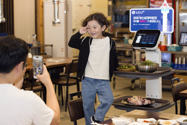 새벽숯불가든 부산대신점 고객이 부산 엑스포 유치 응원 판넬이 부착된 U+서빙로봇과 함께 기념사진을 촬영하는 모습